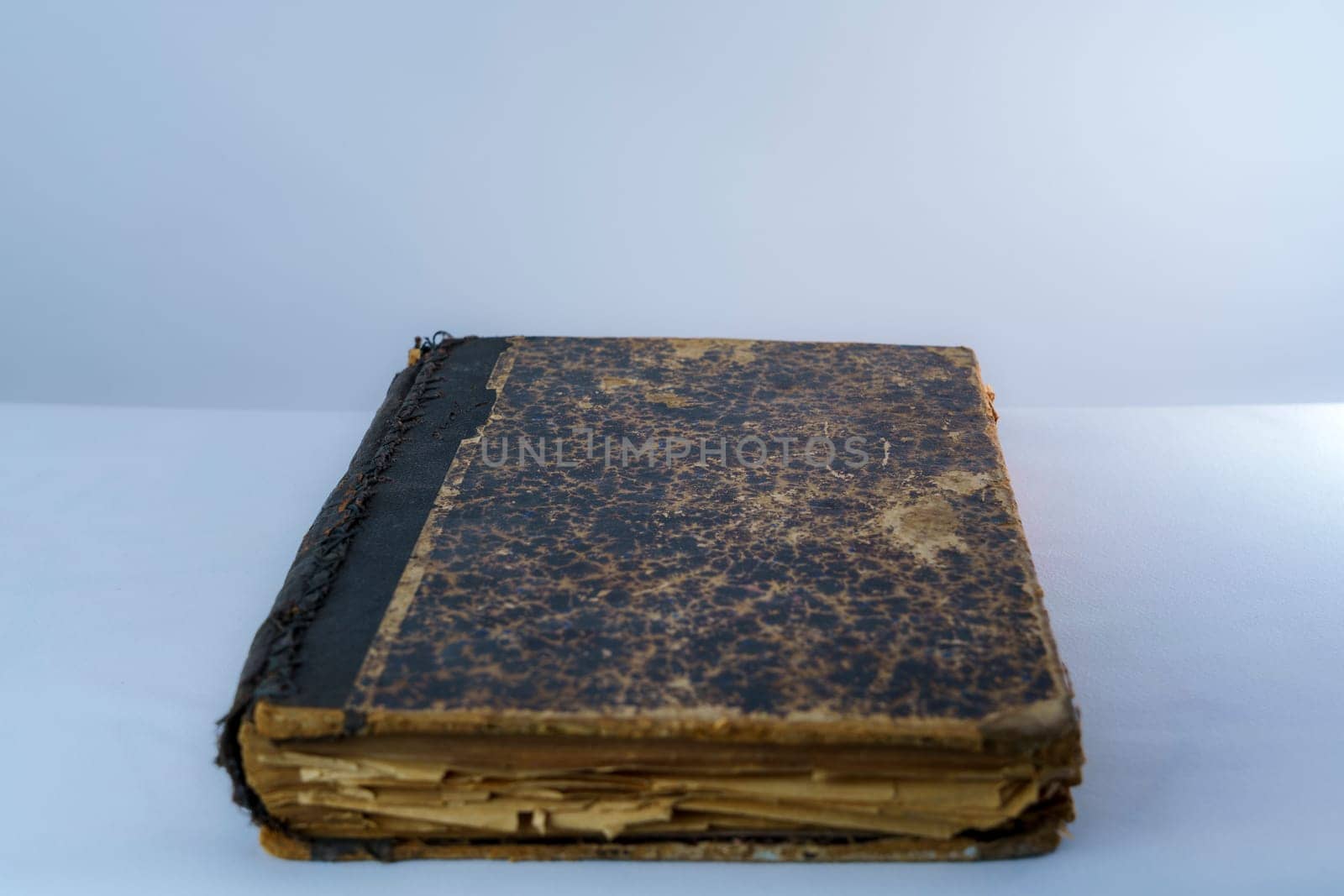 A vintage antique book with a damaged cover and aged, yellowed pages lying on a white surface. Perfect for history, literature, or nostalgia-related projects