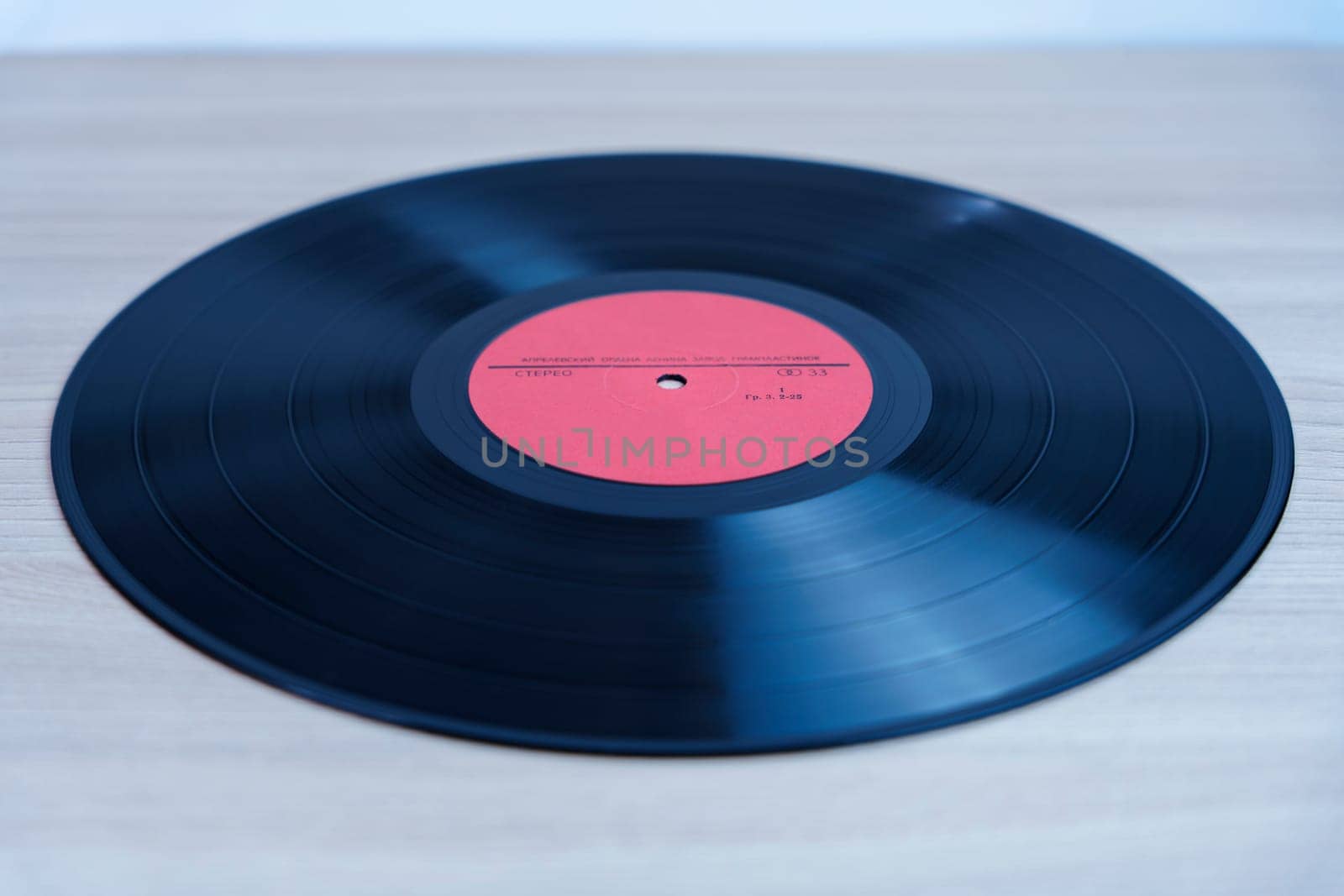 Classic black vinyl record with a red label lying on a wooden background. A nostalgic symbol of analog music, retro sound, and vintage audio formats