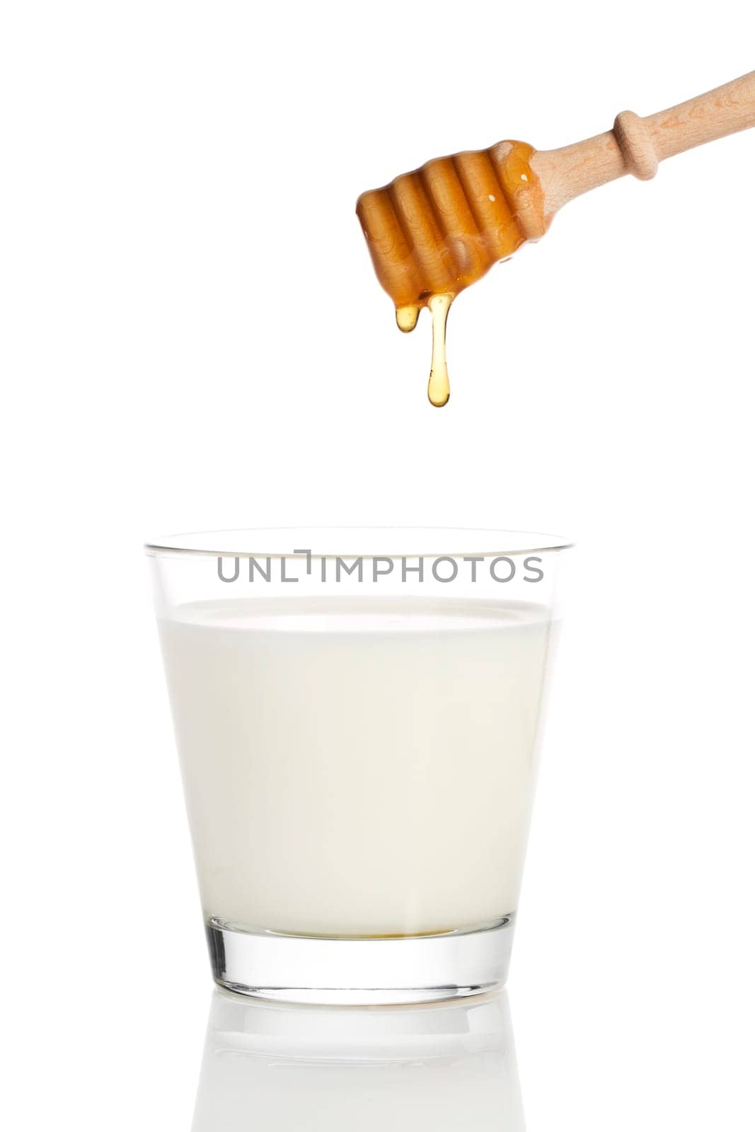 Honey dripping from a honey spoon into a glass of milk against a white background