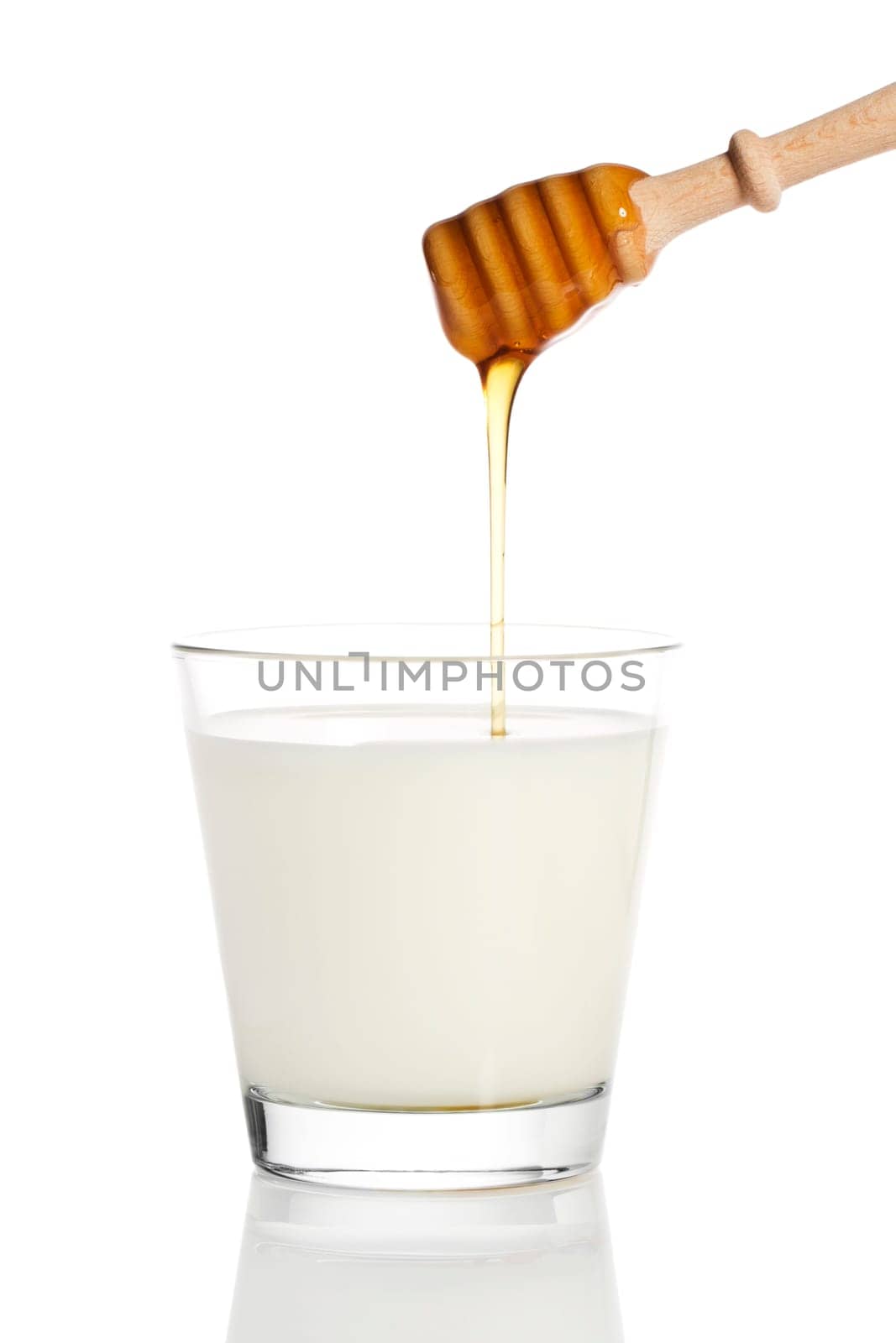 Honey flowing from a honey spoon into a glass of milk against a white background