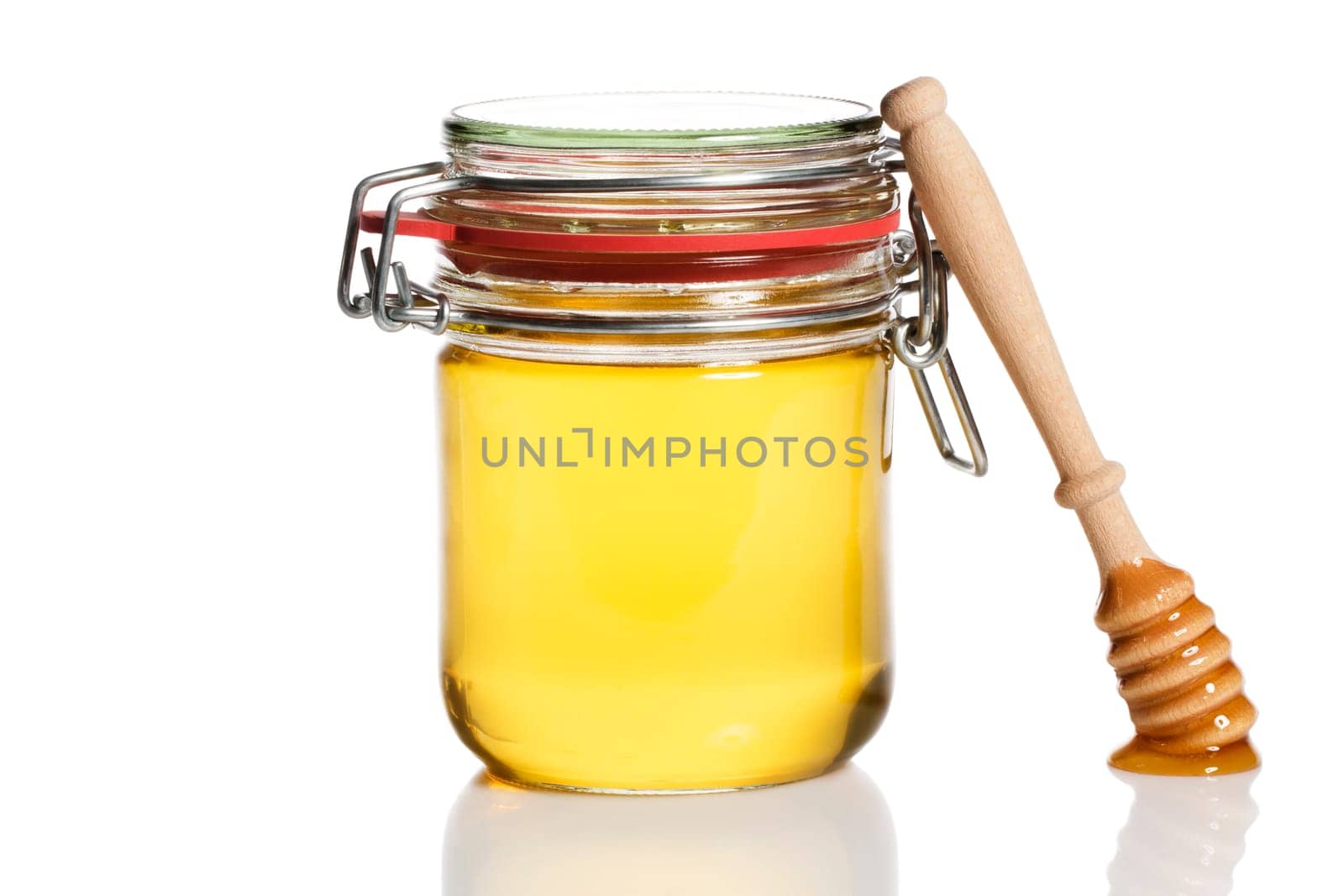 Honey spoon leaning against a jar with honey against a white background
