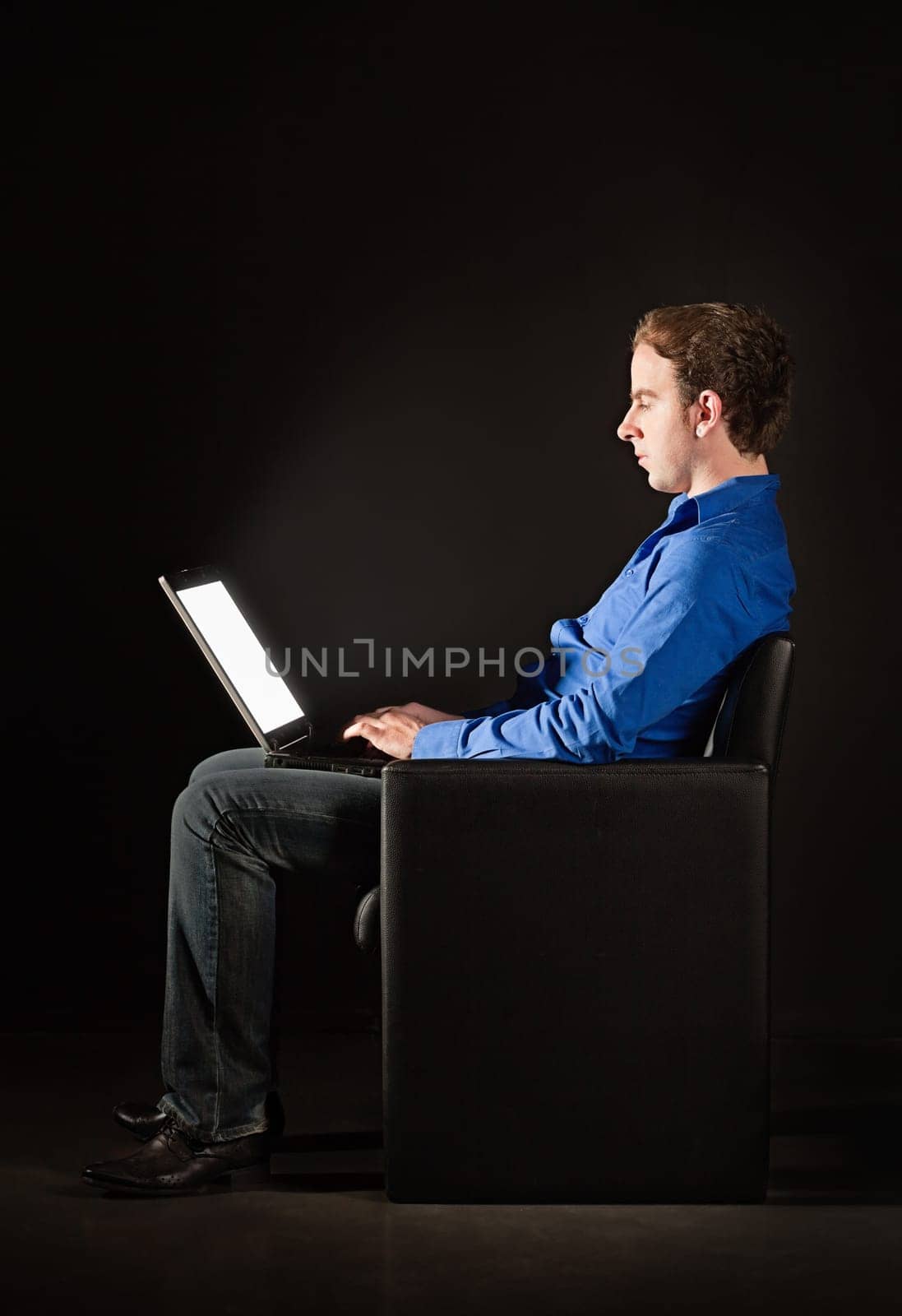 Young man sitting in the darkness with laptop, illuminated by the light from the screen