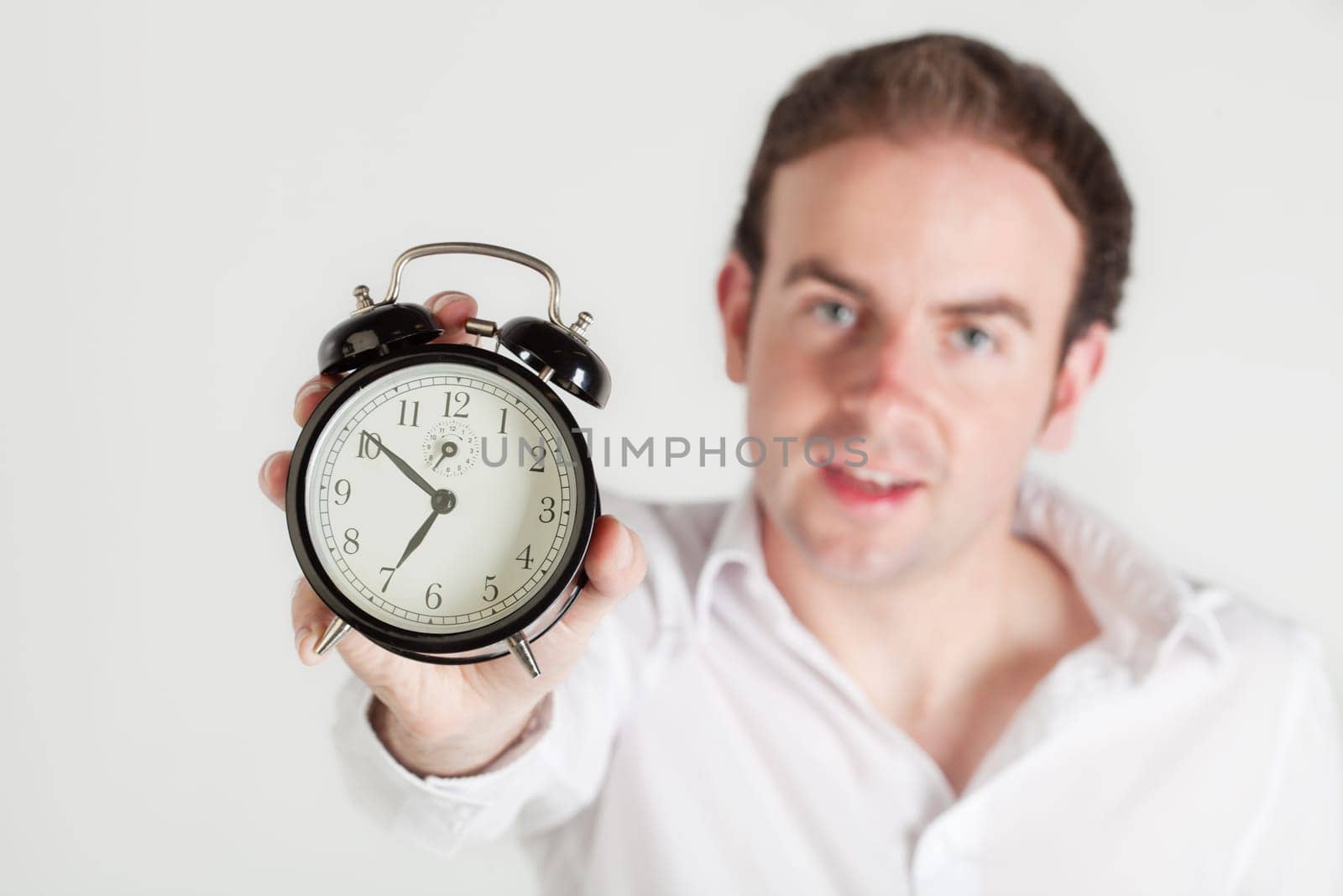 Man holding alarm clock towards the camera. Clock dial in focus, man out of focus.