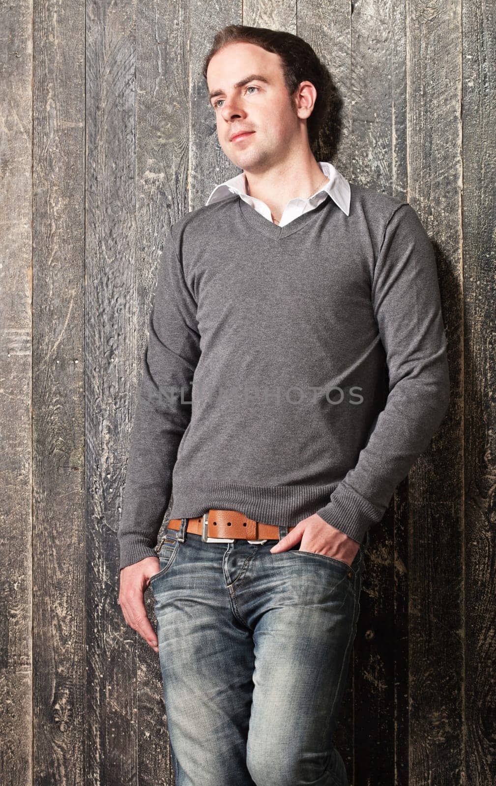 Portrait of a young pensive guy leaning to a dark painted wooden wall