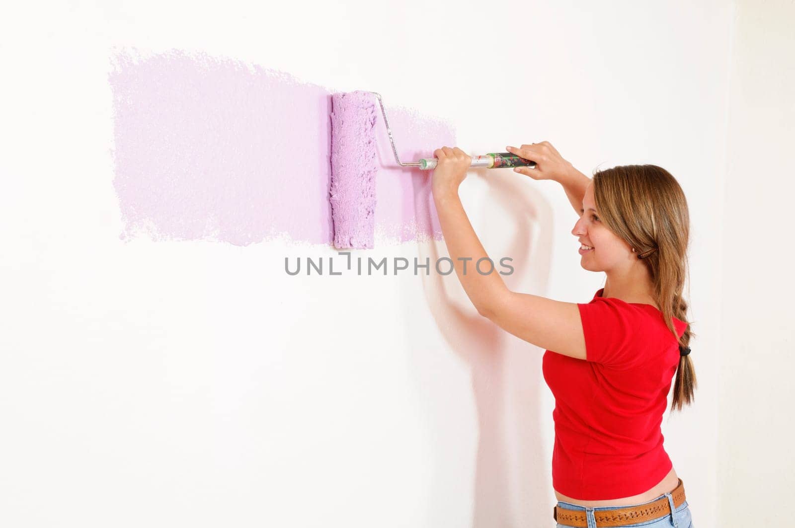 Young woman in a colorful T-shirt paints her first apartment with a paint roller.