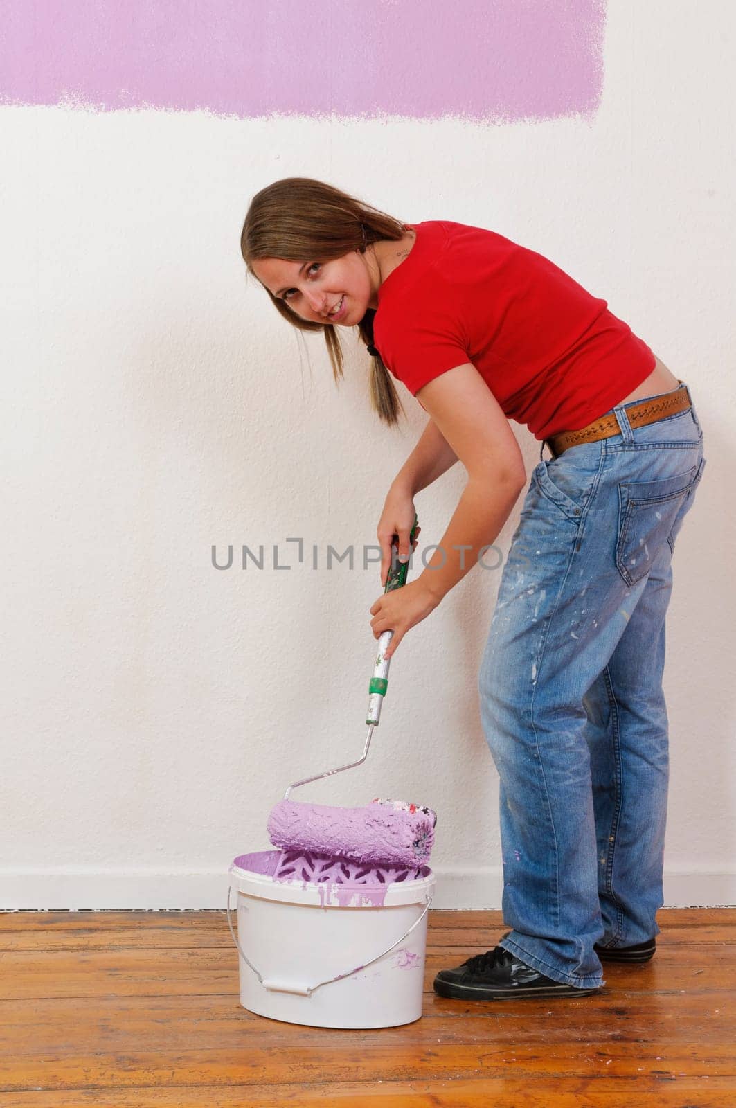 Young woman in a colorful T-shirt paints her first apartment with a paint roller.