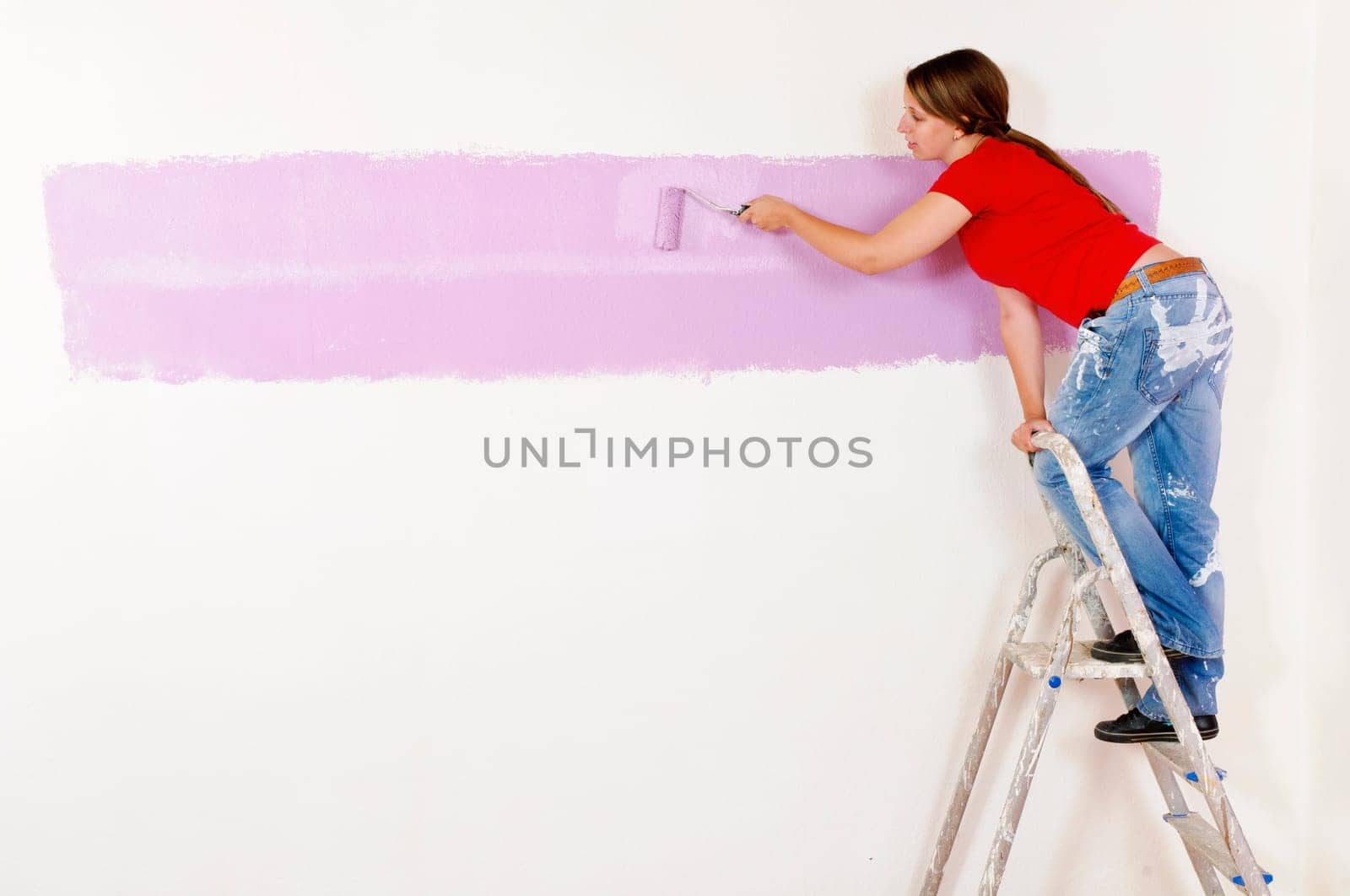 Young woman in a colorful T-shirt paints her first apartment with a paint roller.