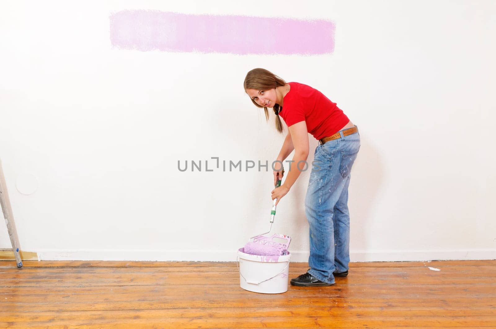 Young woman in a colorful T-shirt paints her first apartment with a paint roller.