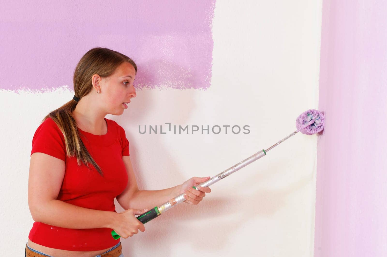 Young woman in a colorful T-shirt paints her first apartment with a paint roller.