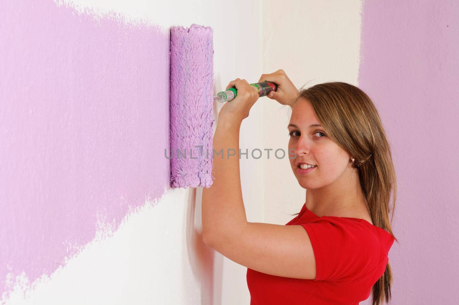 Young woman in a colorful T-shirt paints her first apartment with a paint roller.