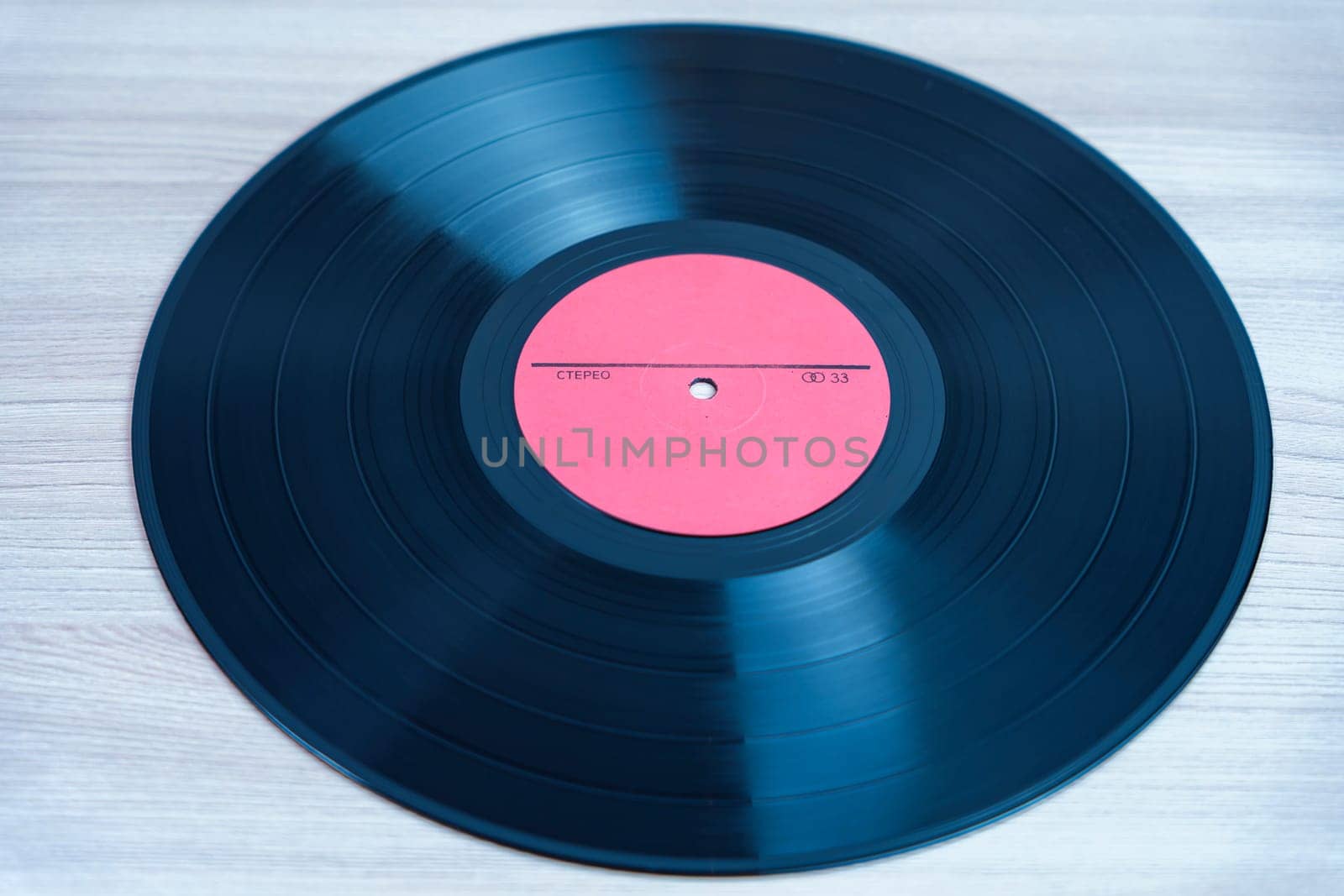Classic black vinyl record with a red label lying on a wooden background. A nostalgic symbol of analog music, retro sound, and vintage audio formats