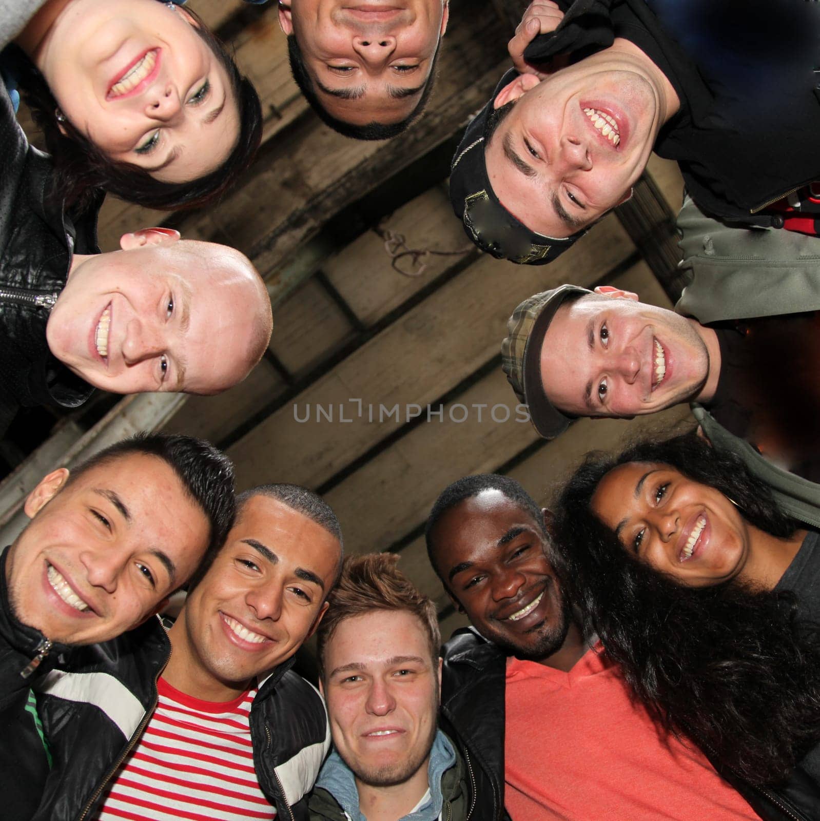 Ten cheerful students of different nationalities stand in a circle and look down laughing