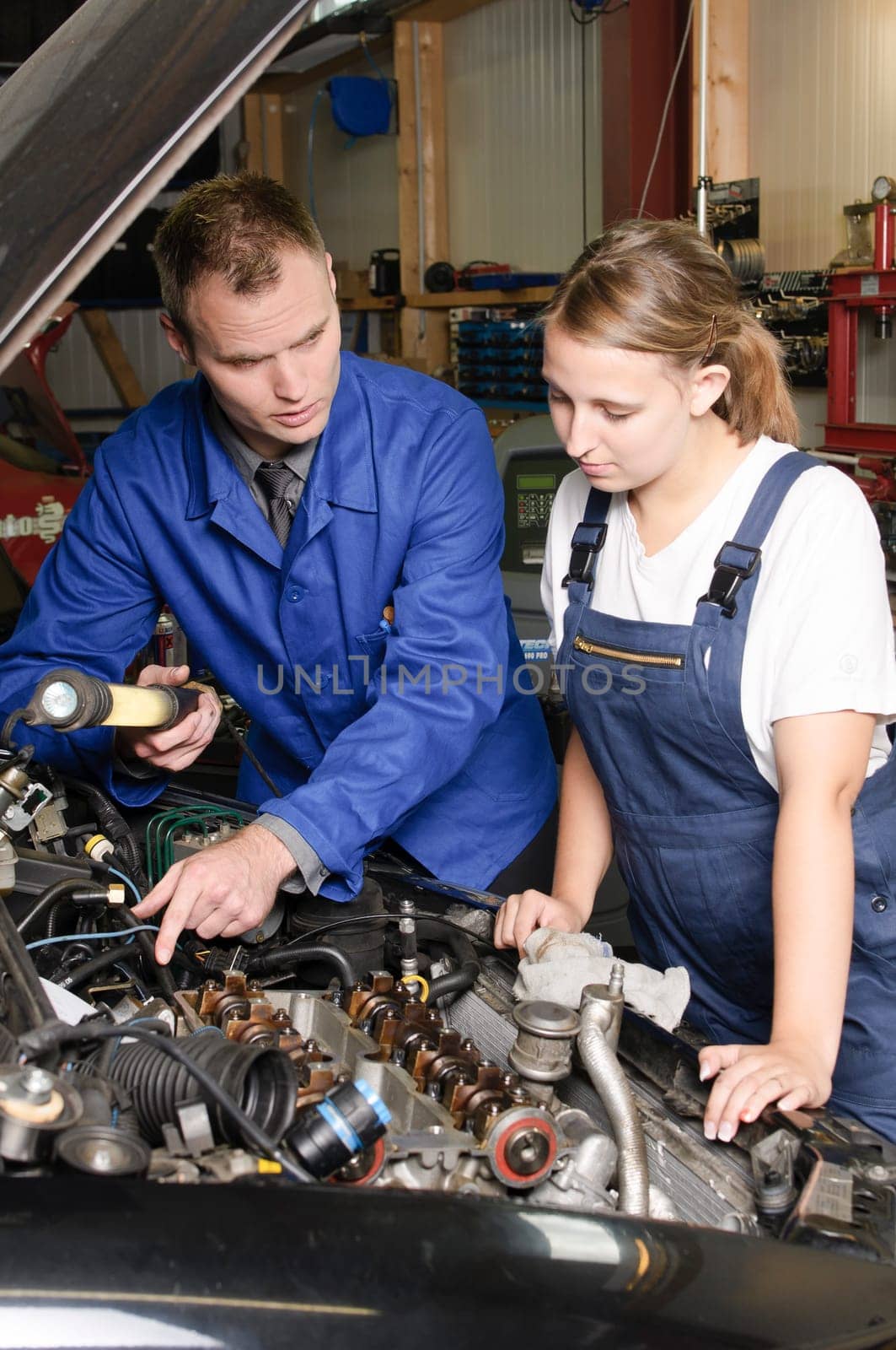 The master craftsman explains to the trainee the work on the engine compartment in the car workshop