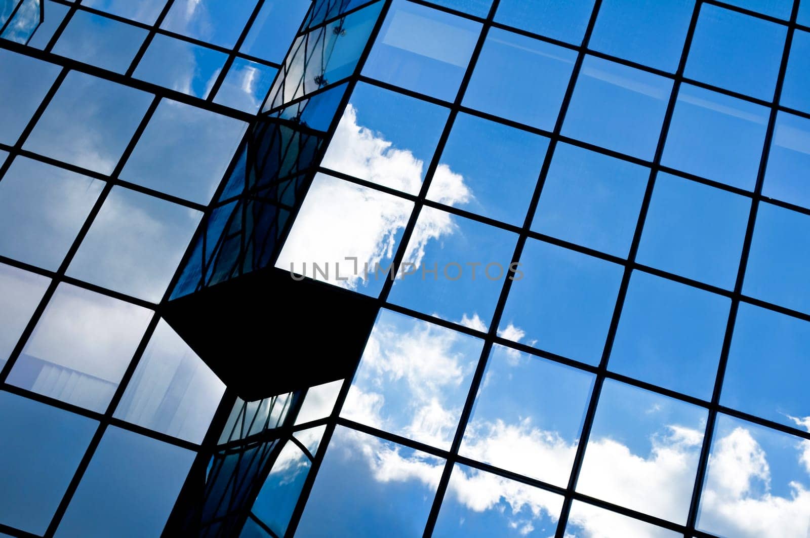 Modern glass office building with clouds and sky reflections.