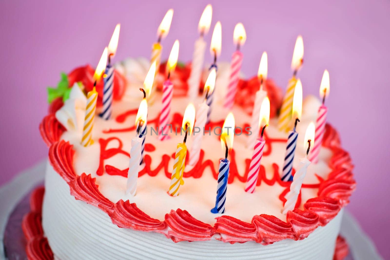 Birthday cake with burning candles and icing on pink background