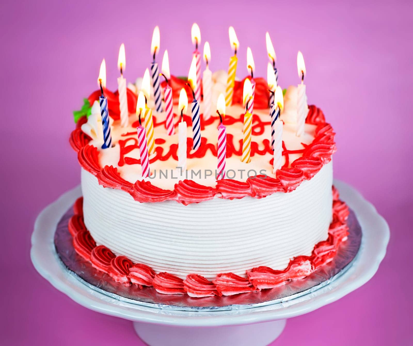 Birthday cake with burning candles on a plate on pink background