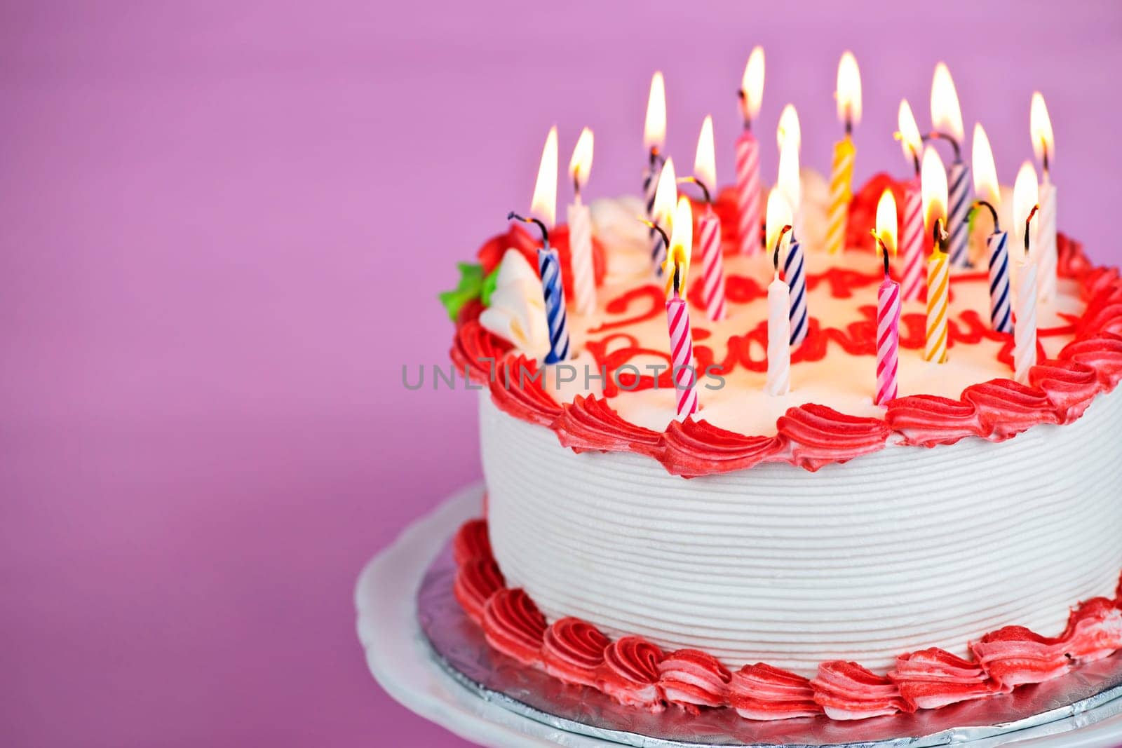 Birthday cake with burning candles on a plate on pink background