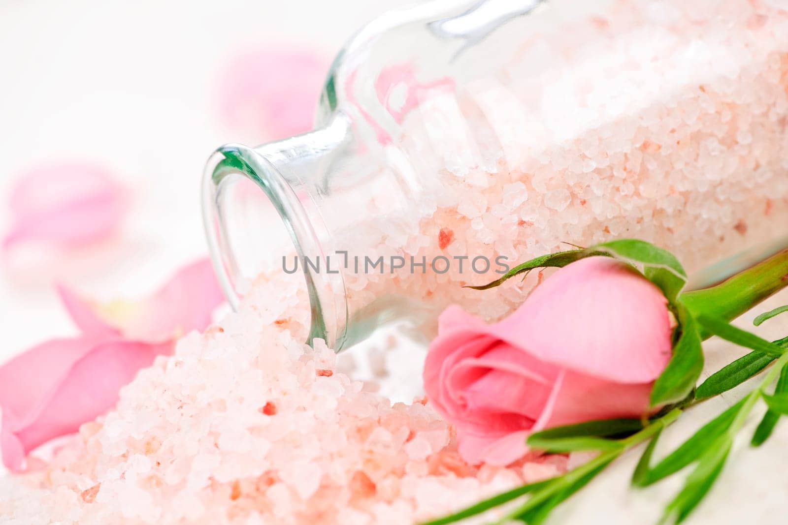 Pink bath salts in a glass jar with flowers and herbs