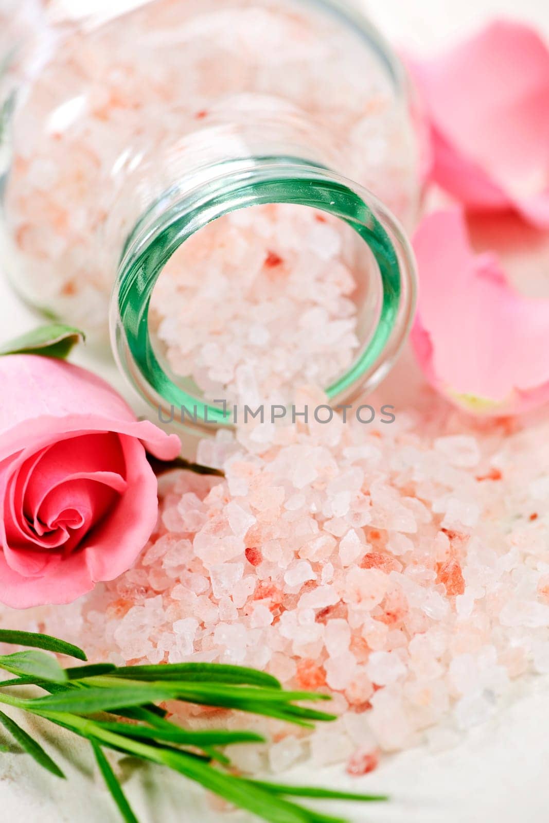 Pink bath salts in a glass jar with flowers and herbs