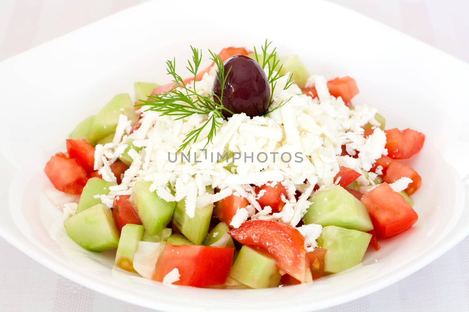 Fresh Greek salad with tomatoes, cucumber, onion, feta cheese and olive on top.