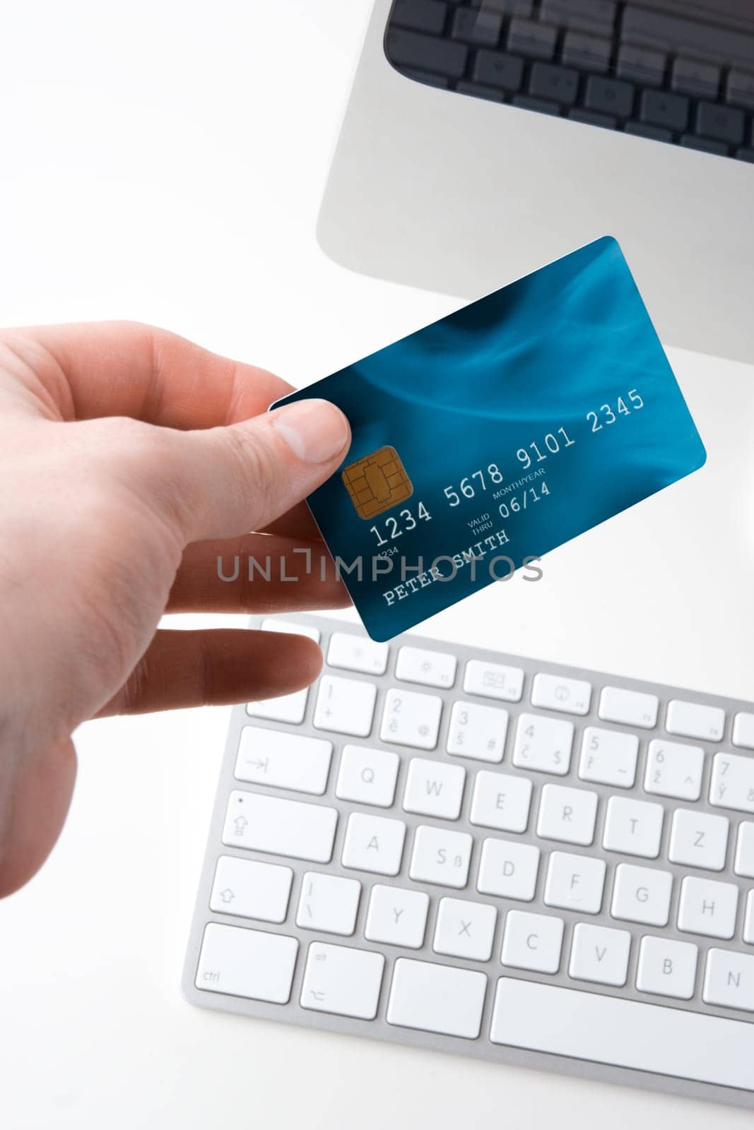 Hand with credit card and computer - electronic payment concept. Focused on credit card. I am author of image used on credit card and used data are fictitious.