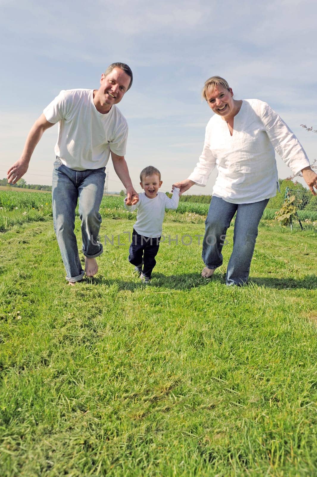 Young family with toddler running together across the field