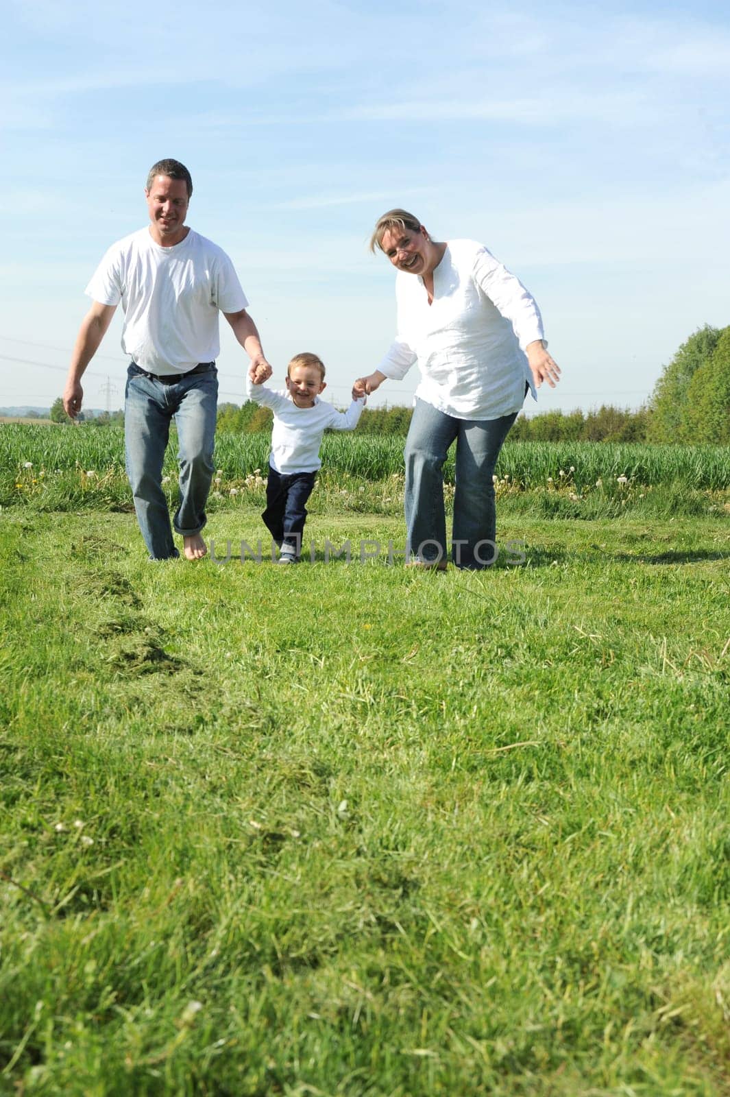 Young family with toddler running together across the field