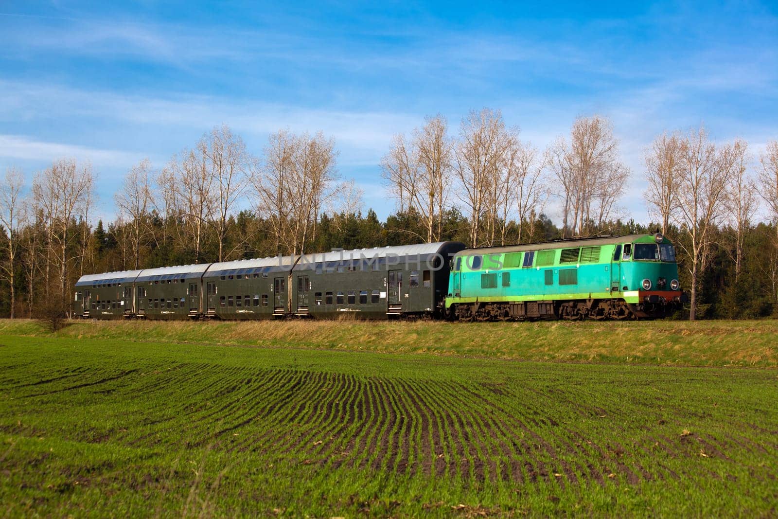 Passenger train hauled by the diesel locomotive passing the sunny landscape