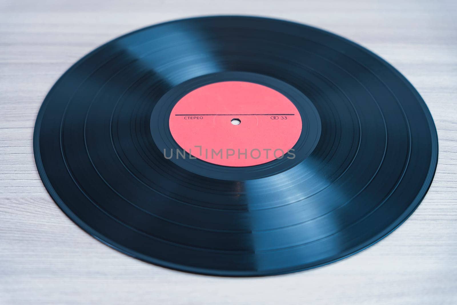 Classic black vinyl record with a red label lying on a wooden background. A nostalgic symbol of analog music, retro sound, and vintage audio formats
