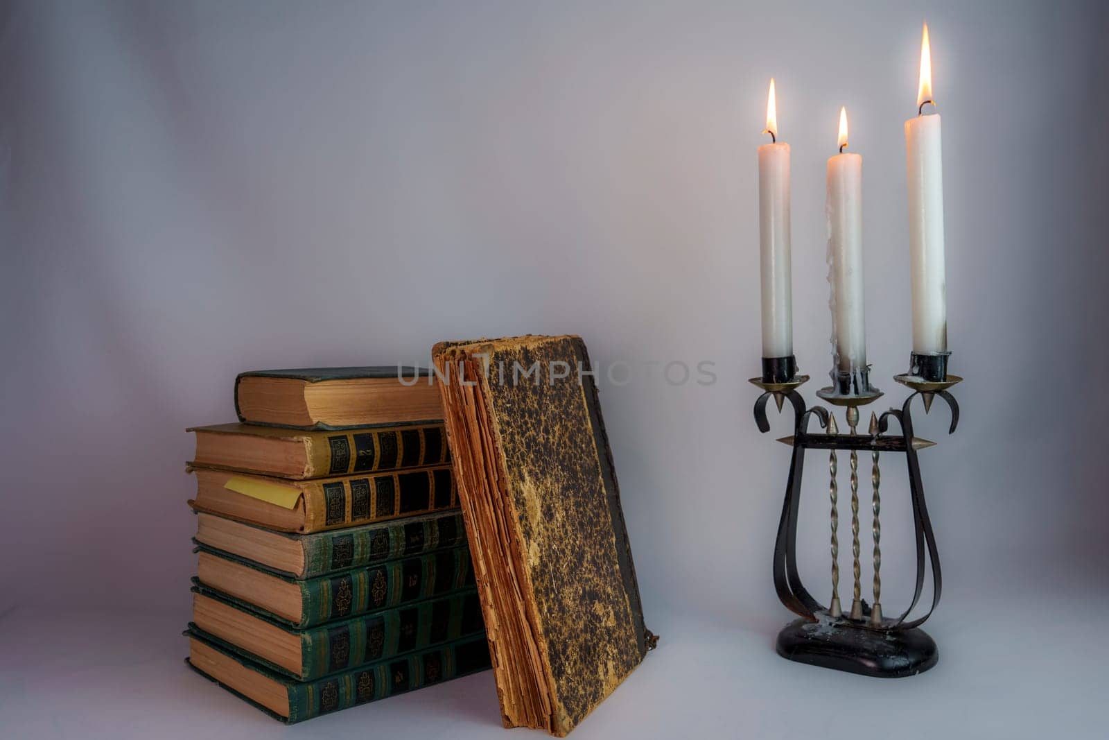 A stack of vintage hardcover books with one book partially open, next to an ornate antique candelabrum with burning candles, creating a nostalgic and elegant atmosphere