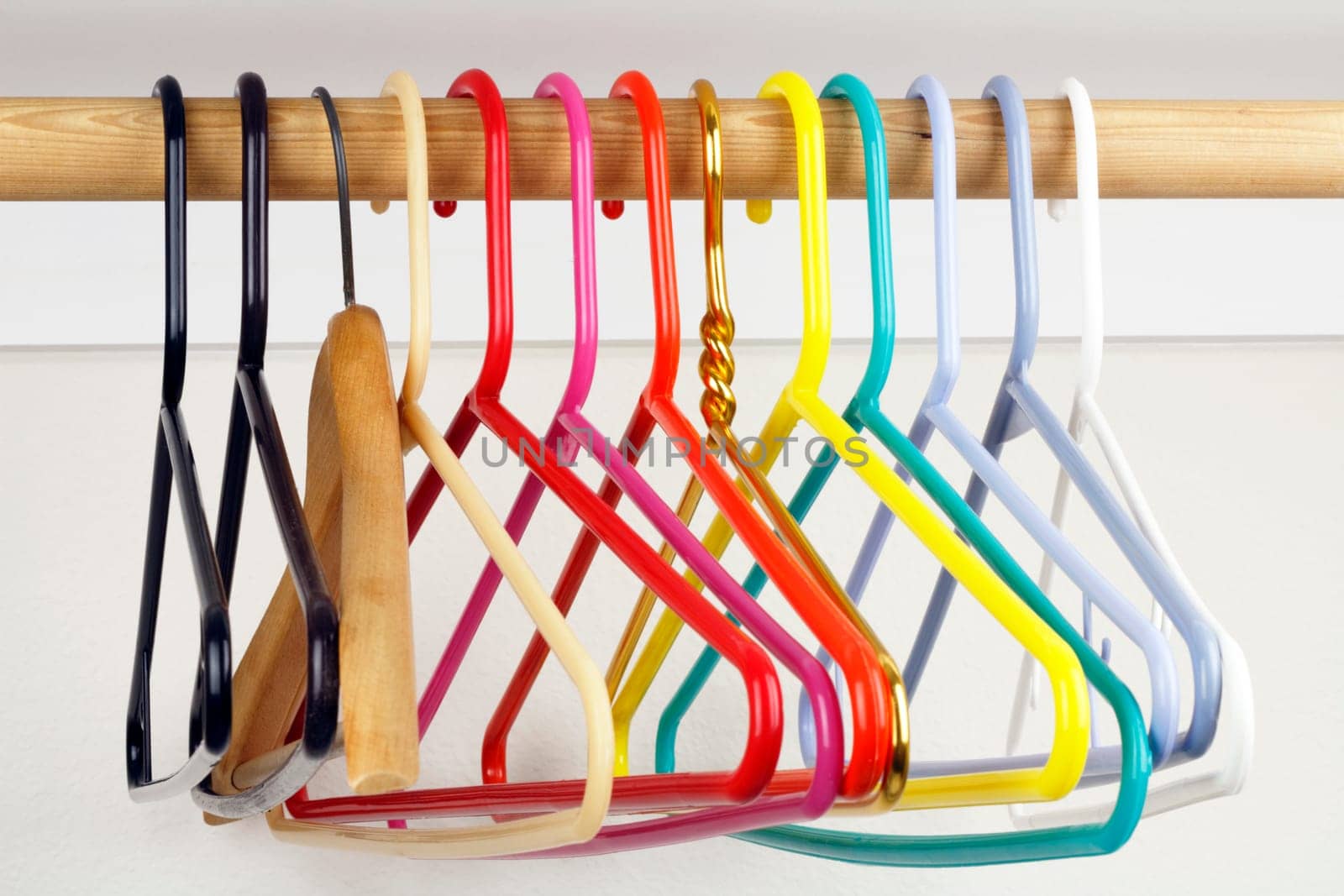 A colorful variety of clothes hangers on a wooden rod.