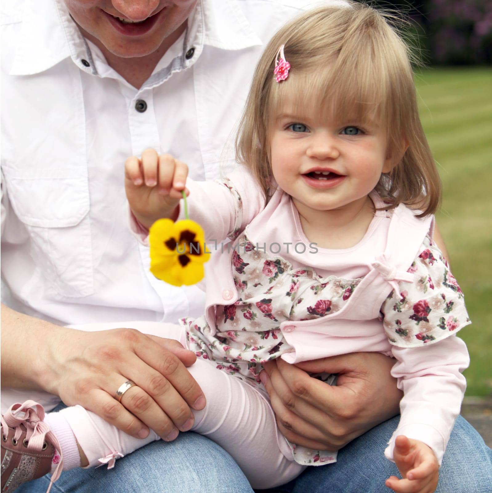 Young father with child. The child holds a flower towards the camera - square