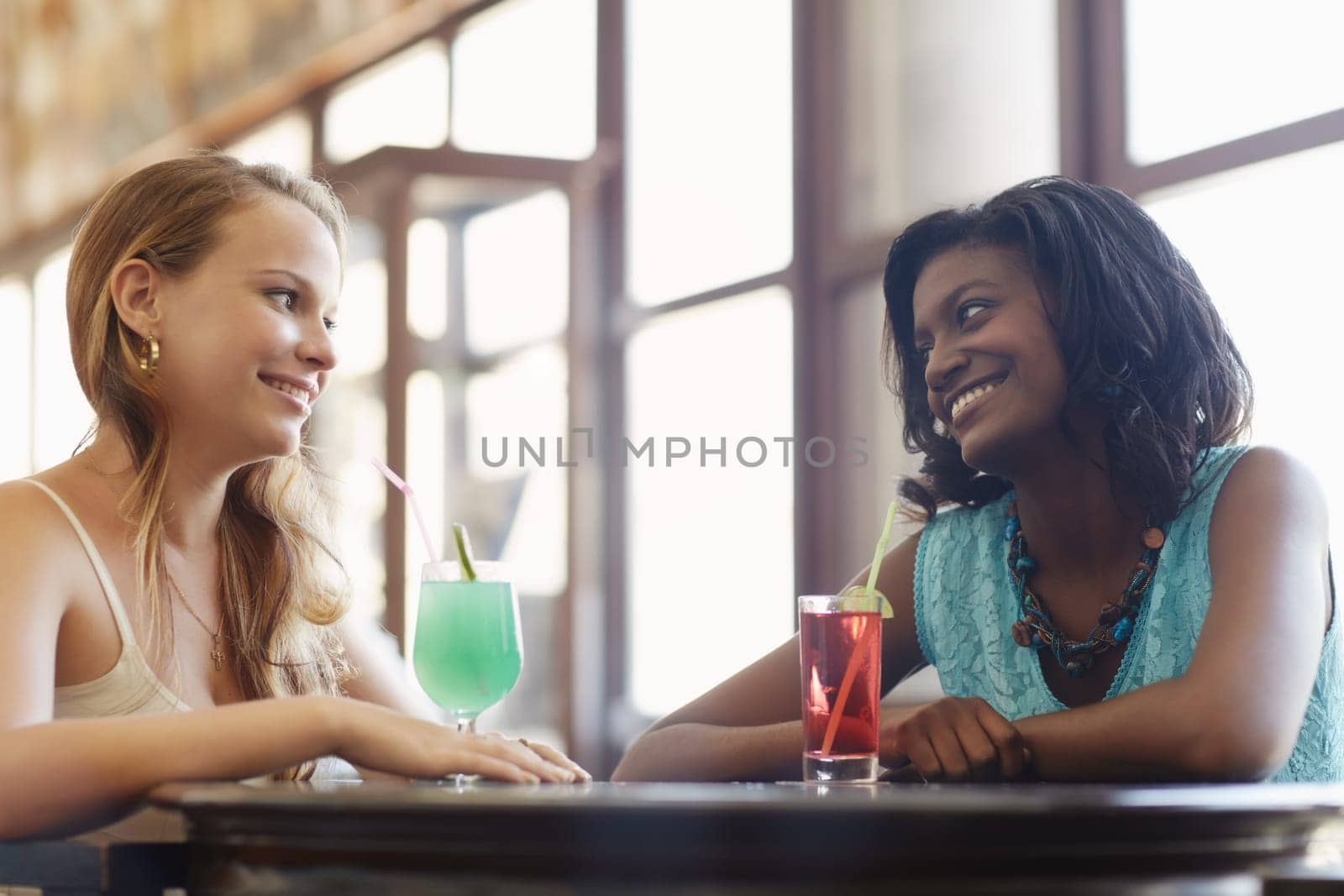 african and latin american female friends drinking cocktails and talking in a pub. Horizontal shape, side view, waist up