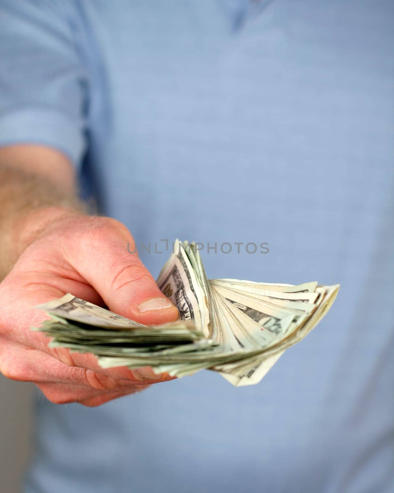 Hand and torso of a man in a blue shirt giving about $1,000. in cash to viewer.
