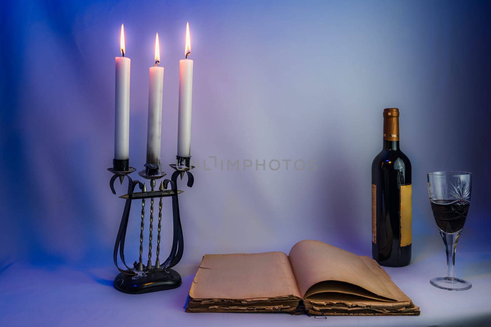 An open vintage book with aged pages, an antique candelabrum with burning candles, a wine bottle, and a filled glass, set in dim lighting, creating a mysterious and elegant atmosphere