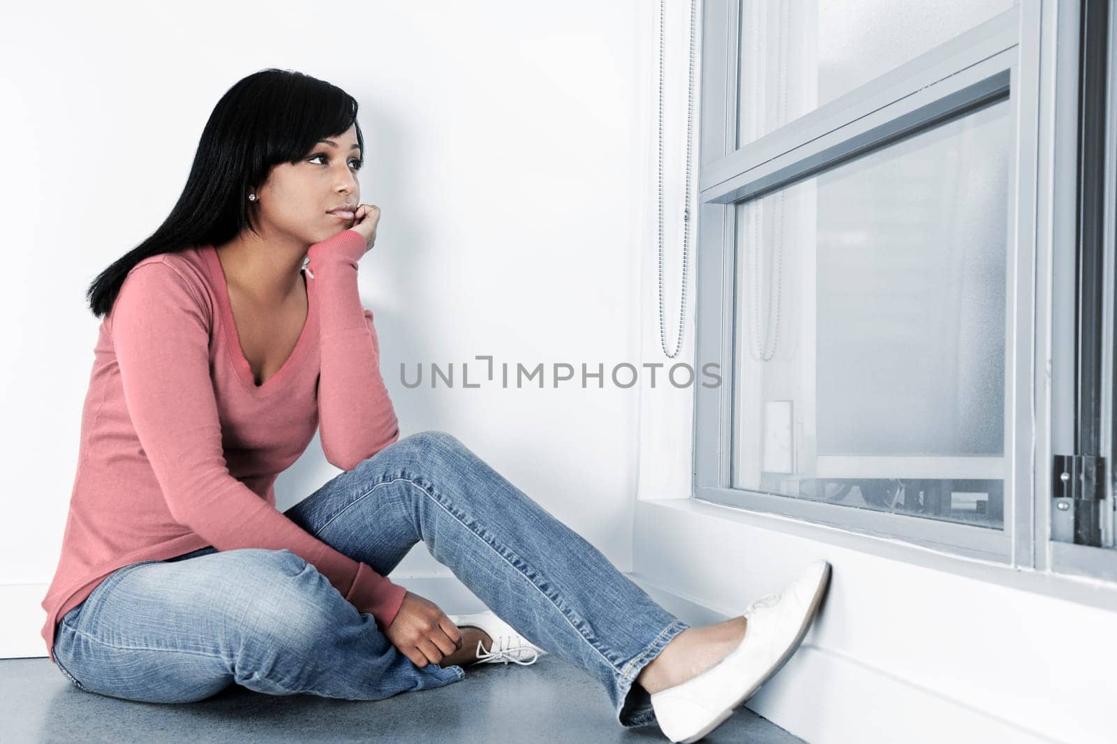 Depressed black woman sitting against wall on floor looking out window