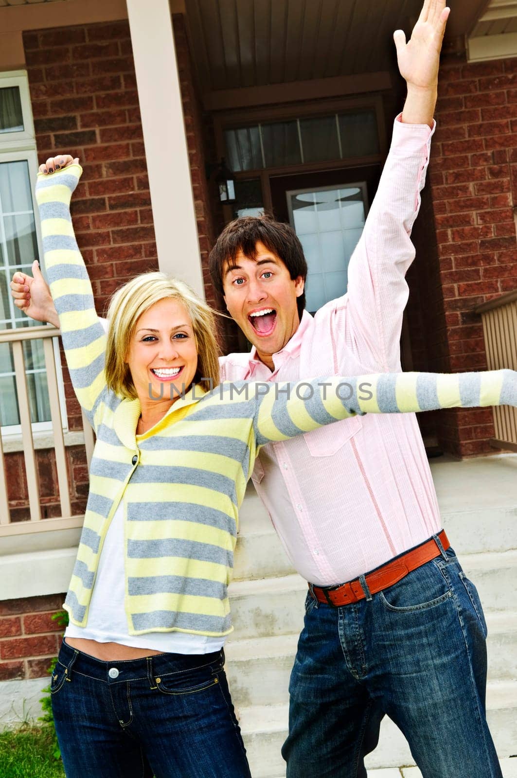 Young excited couple celebrating in front of home