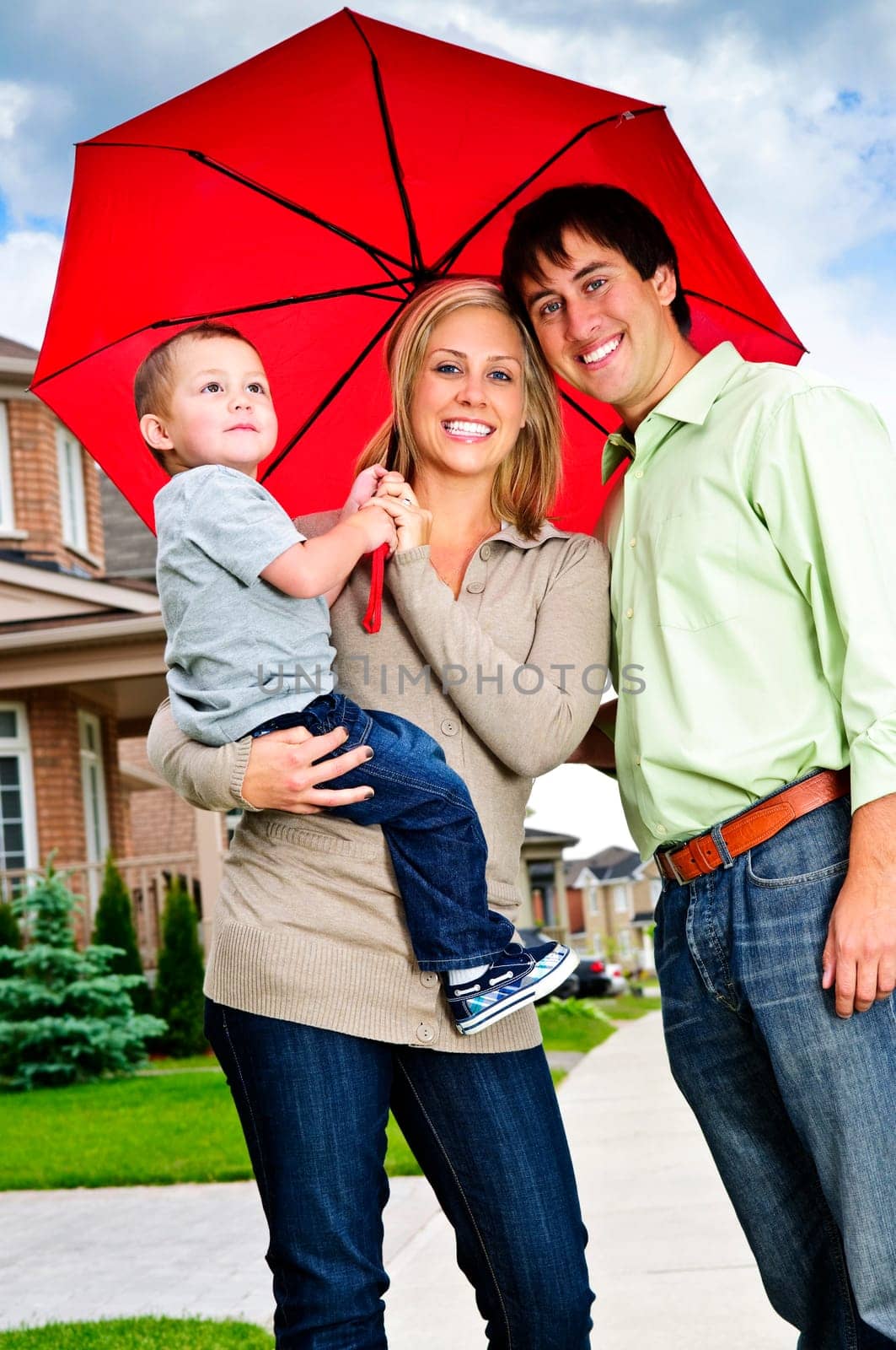 Young happy family under umbrella on sidewalk