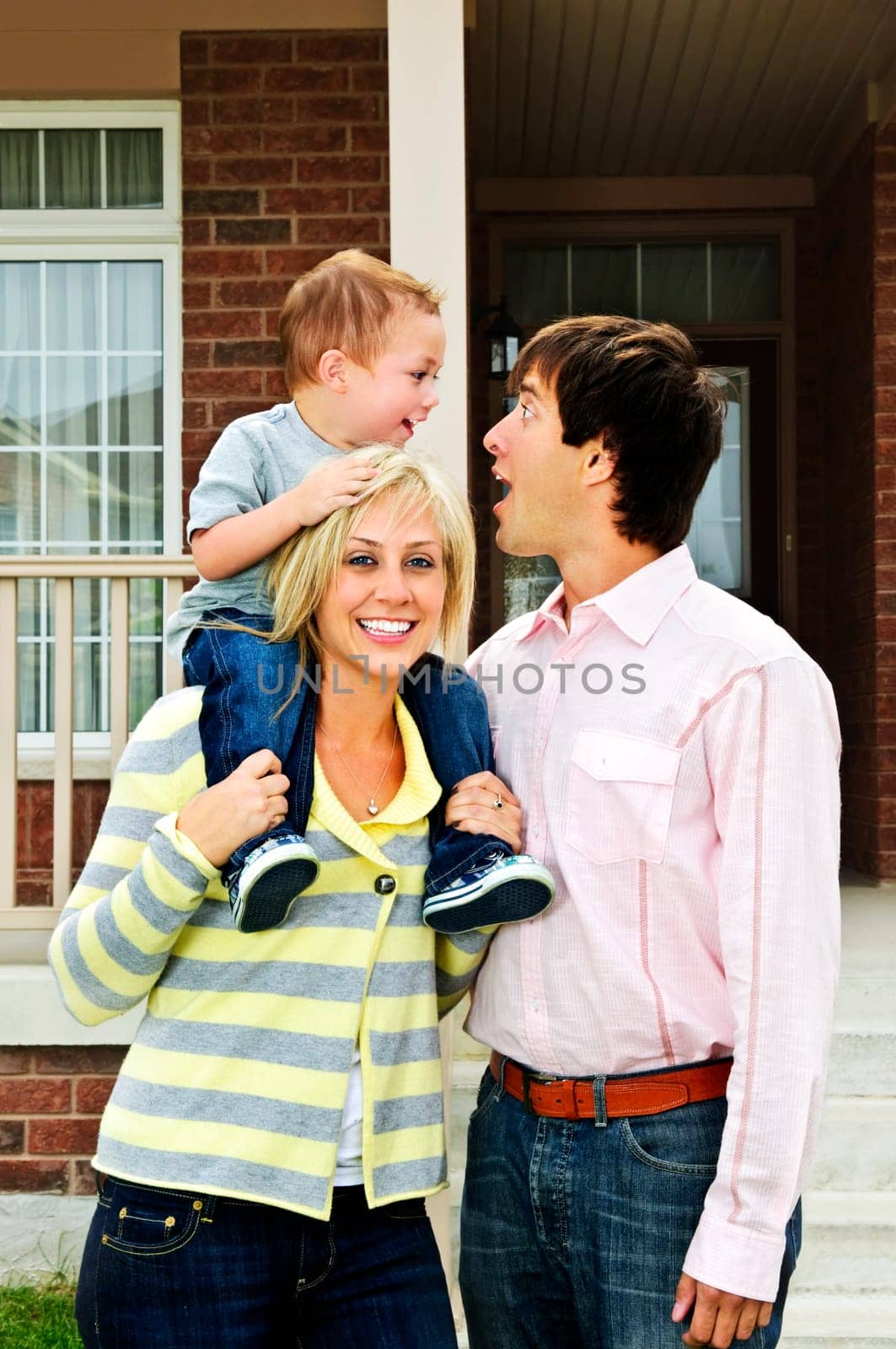 Young happy family standing in front of new home