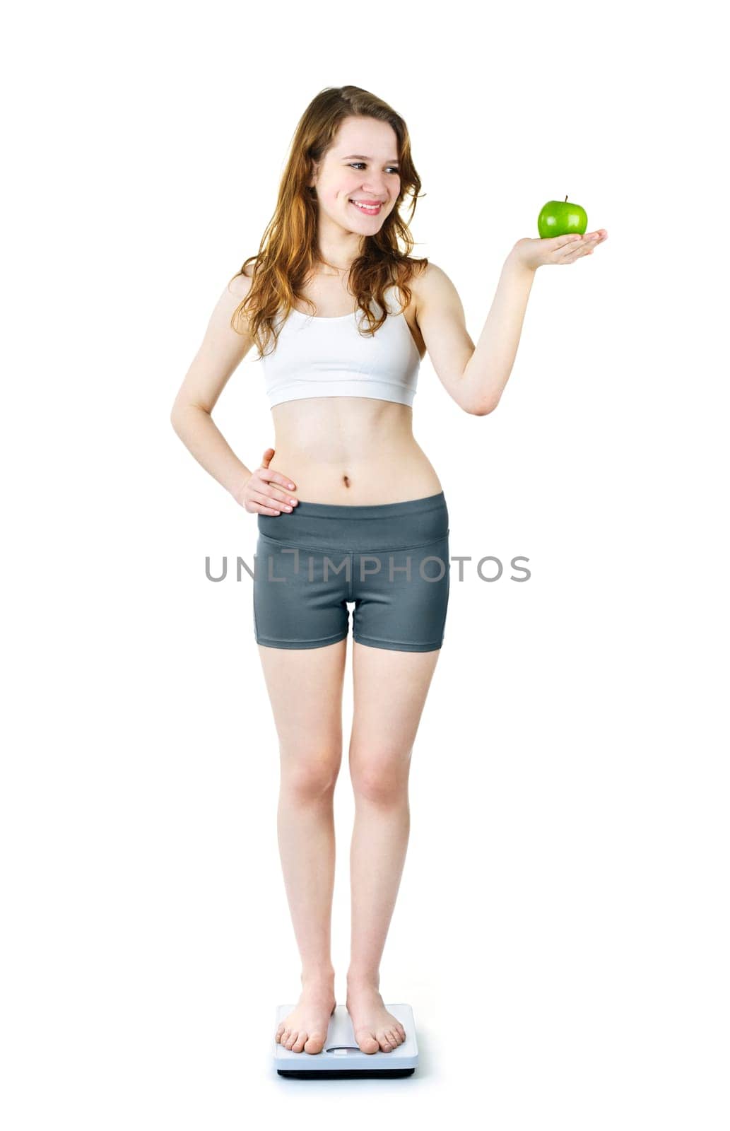 Healthy happy young woman holding green apple standing on bathroom scale