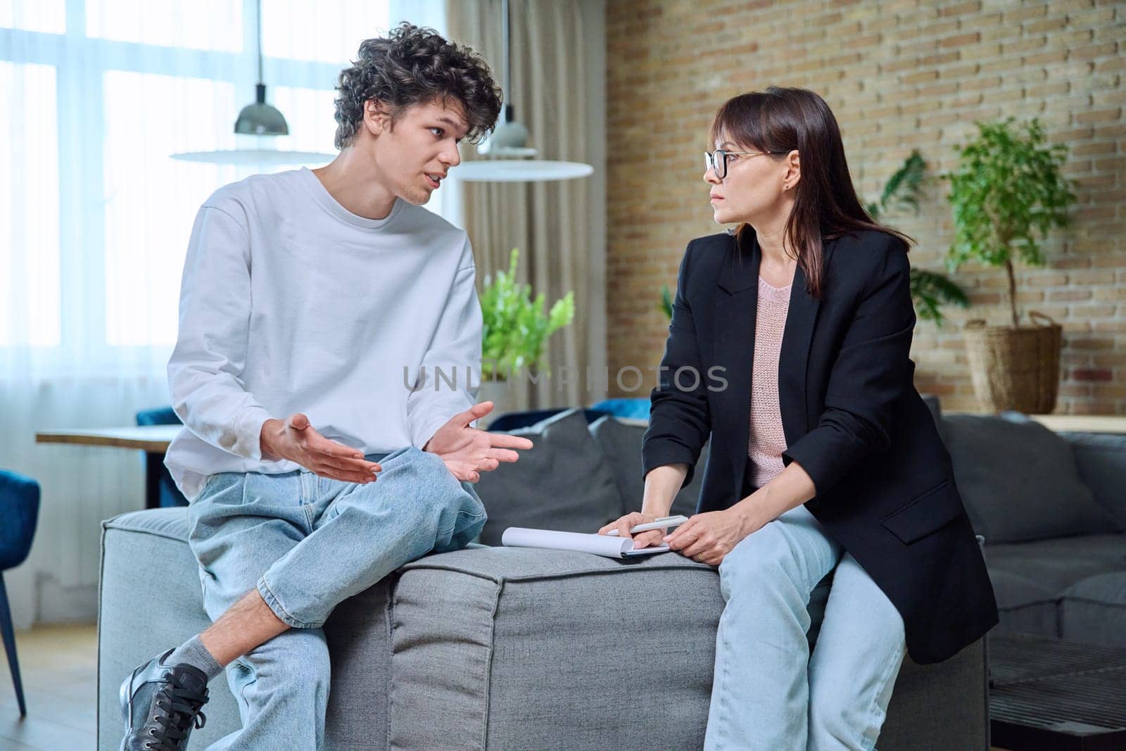 Young 18-20 year old male student communicates with female psychologist counselor at therapy session in office. Mental problems difficulties, professional treatment help support from psychotherapist