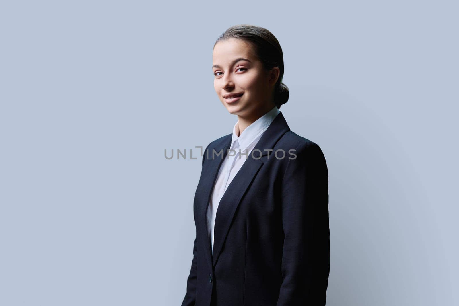 Portrait of confident teenage high school student girl on grey background. Smiling female in formal business attire looking at camera. Education, high school, adolescence concept