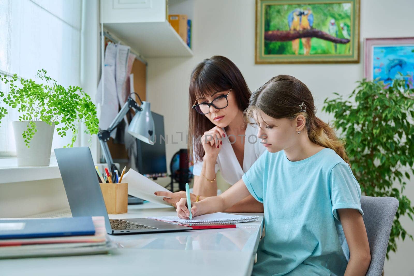 Mother helping preteen daughter to study, looking at laptop computer at desk together at home. Family, home lifestyle, school, education, study, kids concept