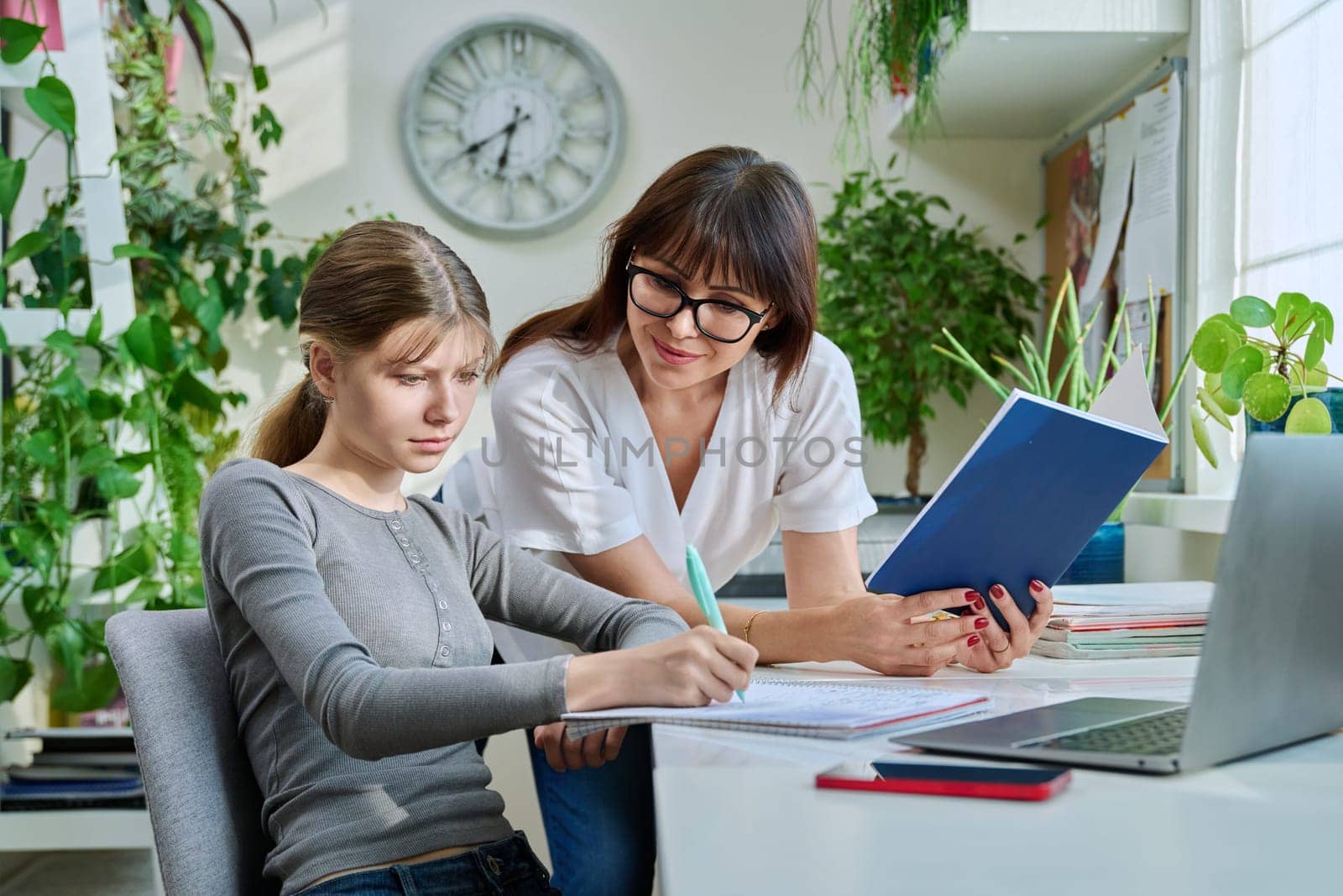 Mother helping preteen daughter to study, looking at laptop at home by VH-studio