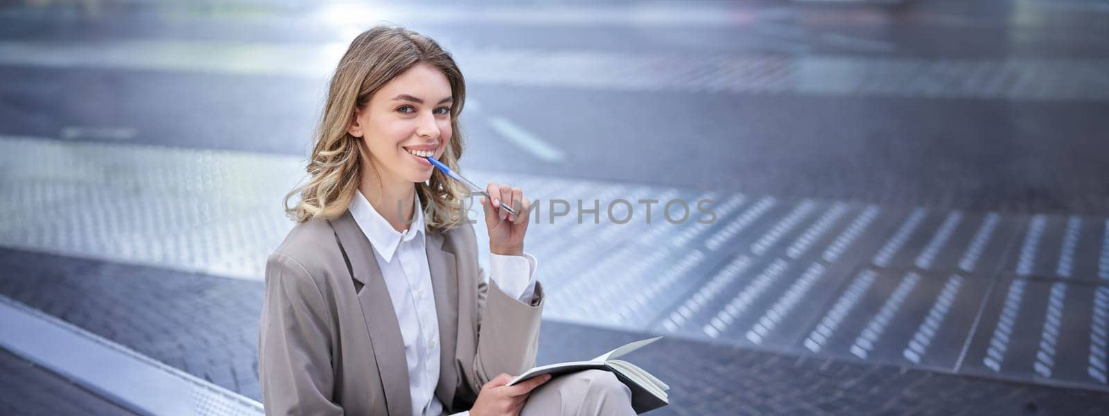 Businesswoman sitting in city centre with notebook and pen. Corporate woman writing down ideas, thinking.