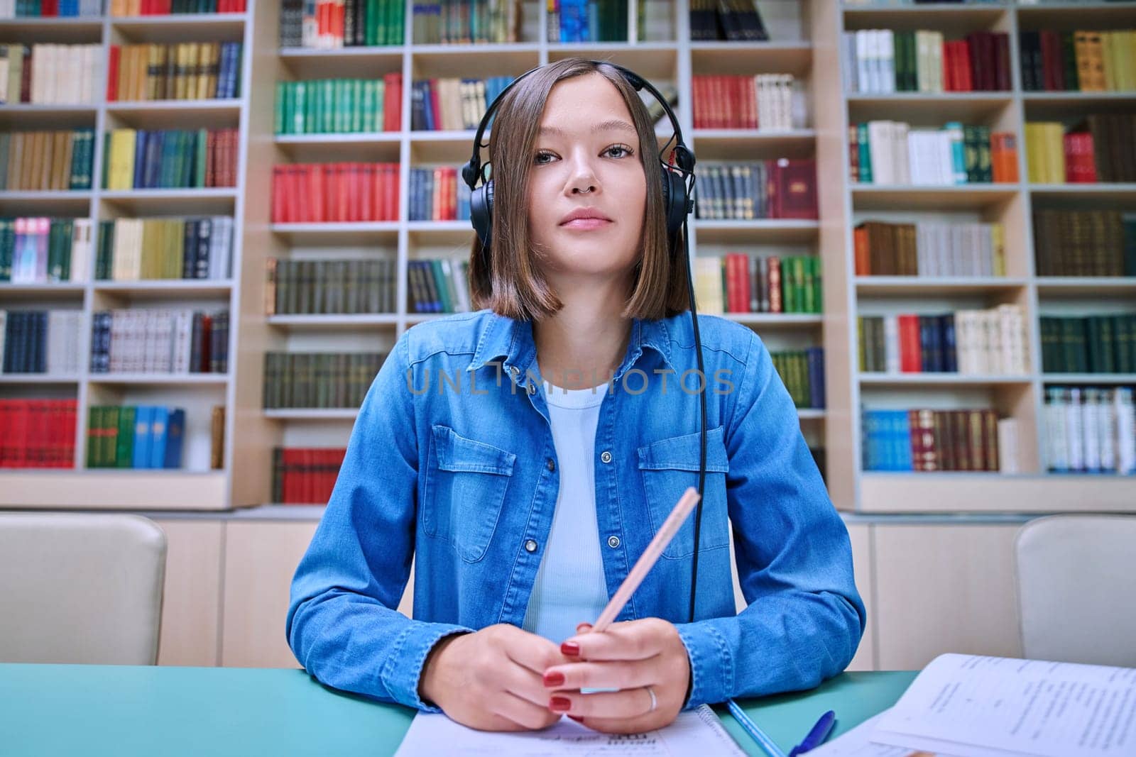 Close-up webcam view of face female student in headphones, inside university library. Young woman looking at camera online chat conference broadcast video recording. Internet technology for learning