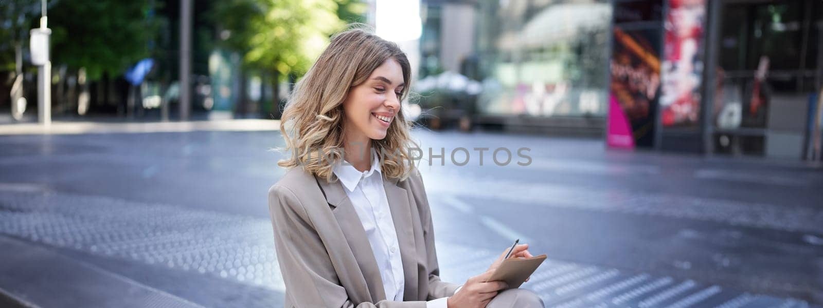 Young businesswoman preparing for speech, interview in company, writing down notes while sitting outside in city centre.