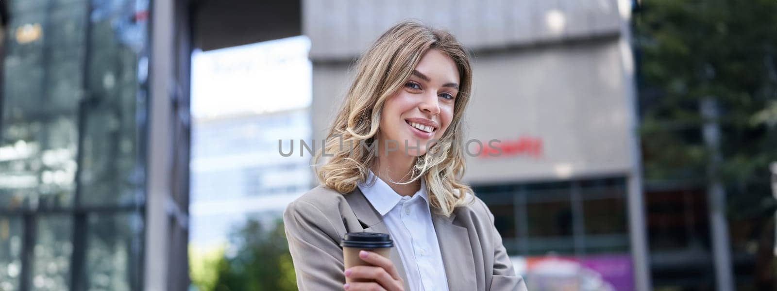 Professional woman standing with coffee in a busy street, smiling at camera by Benzoix