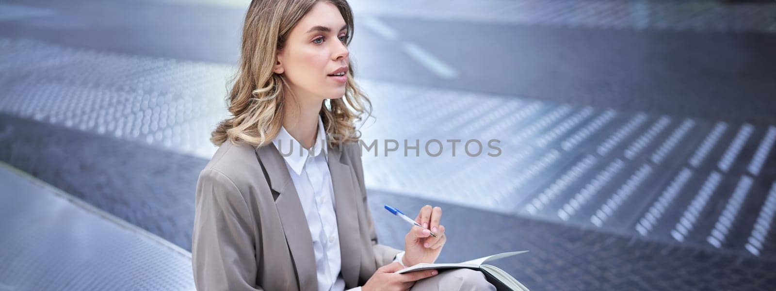 Businesswoman writing down her thoughts, corporate lady sits outdoors, works, brainstorming by Benzoix