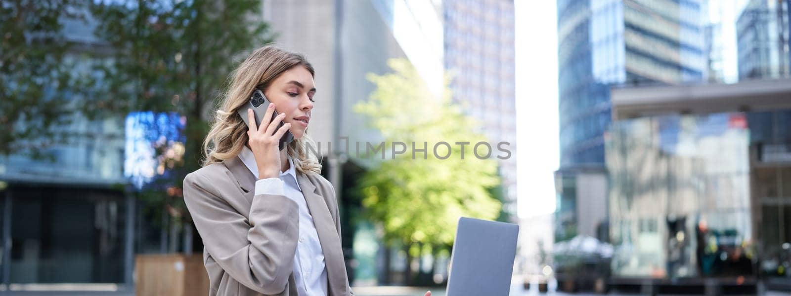 Businesswoman checking diagram and work on laptop, calling someone on mobile phone, sitting outdoors in city centre.